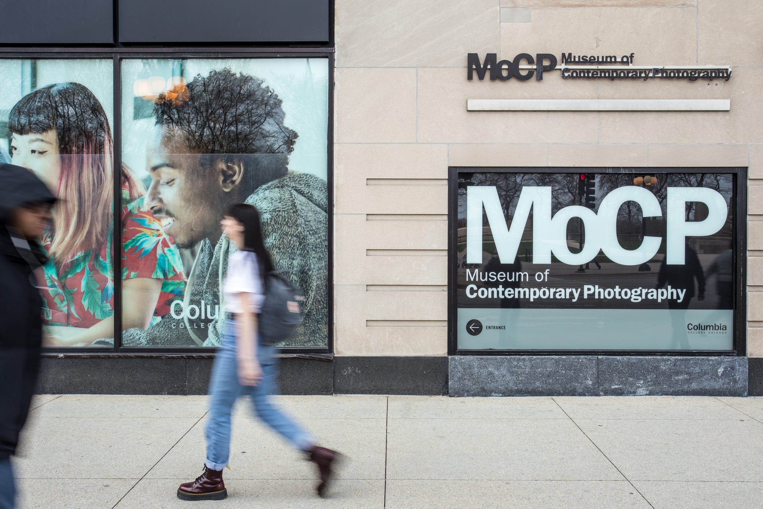 Pedestrians walk past a building with a sign on its facade that reads MoCP, Museum of Contemporary Photography