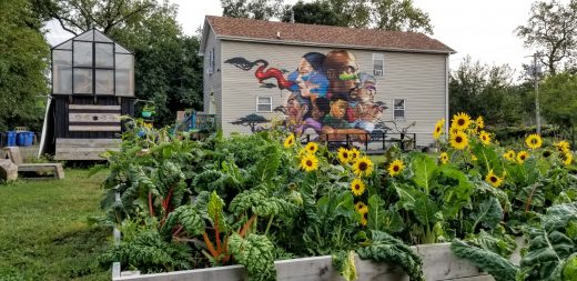 A house with a painted mural on its side, with a lush garden bed in the foreground