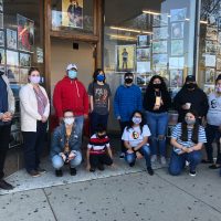 A group of people wearing face masks stand in front of a storefront with photographs in the window.