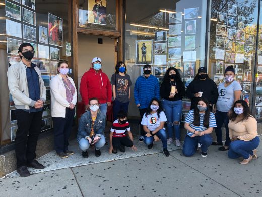 A group of people wearing face masks stand in front of a storefront with photographs in the window.