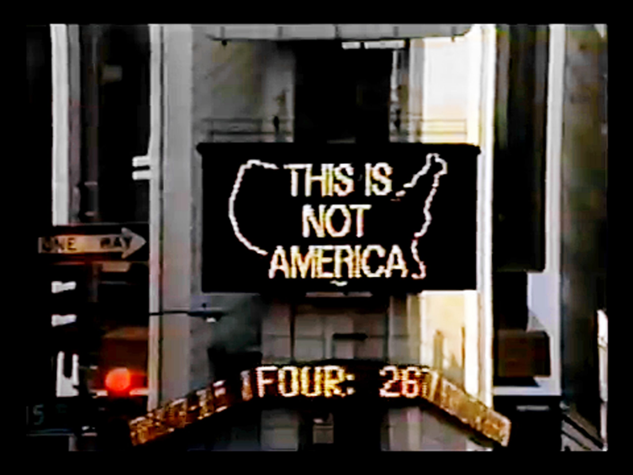 Photograph of lighted billboard with “This is not America” text on the shape of the continental United States. 