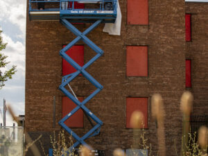 Three people on a scissor lift drape a banner in front of a brick building