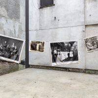 Four photographs of women printed on linen hang on a clothesline in an empty lot