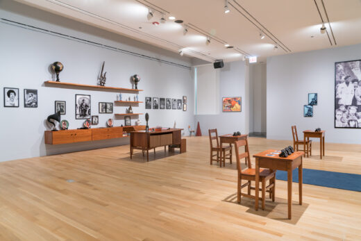 Gallery installation with school desks, photographs, and a collection of items related to the Black Panthers.