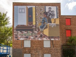 A vinyl mural hangs on the outside wall of a brick building