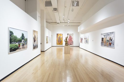 Gallery view with large paintings, photographs and a bronze sculpture in the center of the room