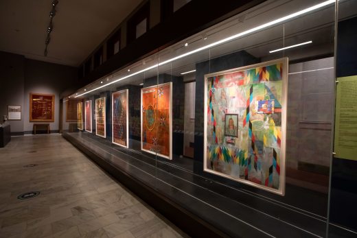 A series of paintings hang behind a glass display case