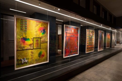 A series of paintings hang behind a glass display case