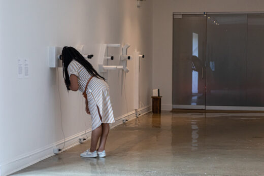 Gallery installation with a person leaning into a wall mounted sculpture.