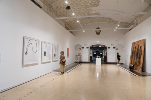 Gallery installation in a long bank corridor featuring a large charcoal on wood panel drawing.