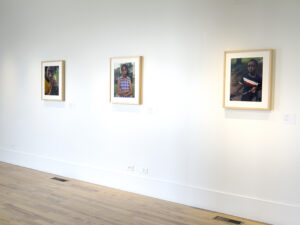 Gallery installation displaying three photographs, each a portrait of a student.