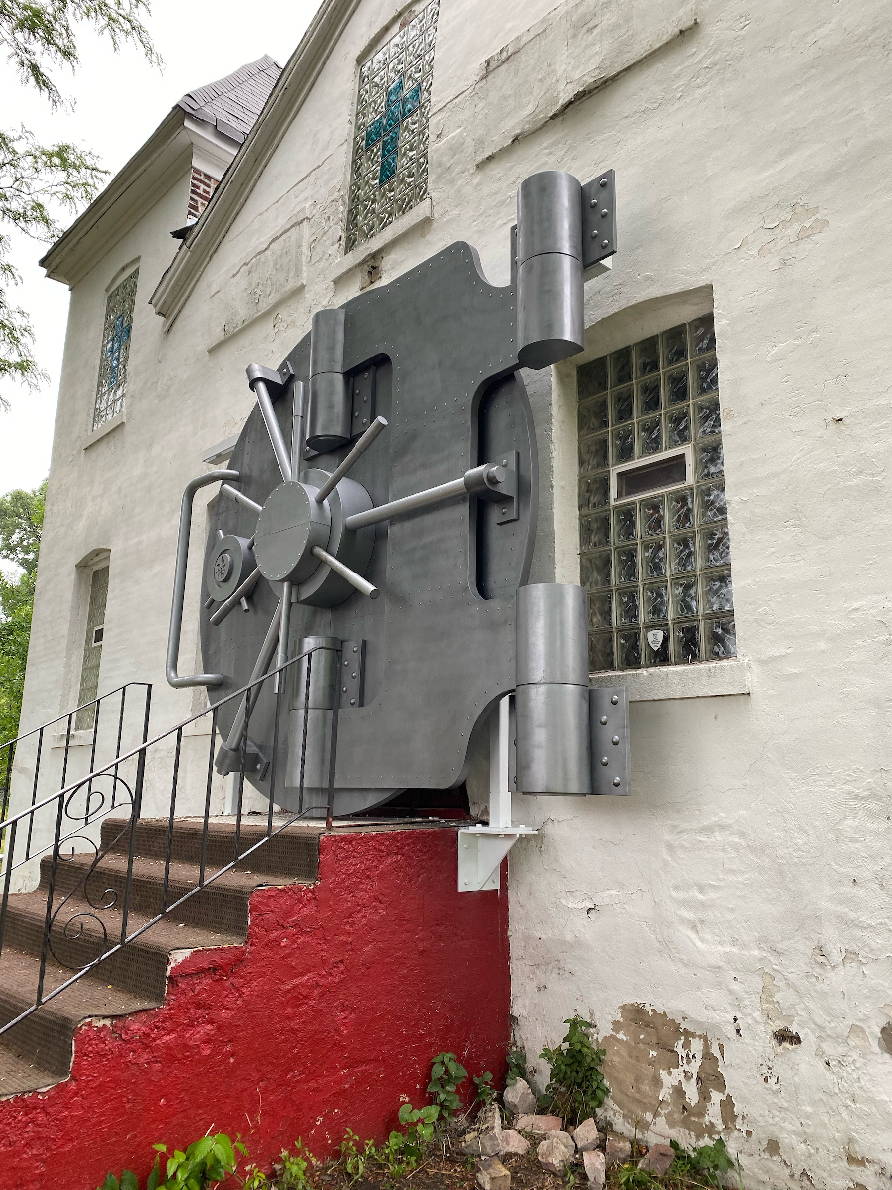 A metal bank vault door is installed on a white building.