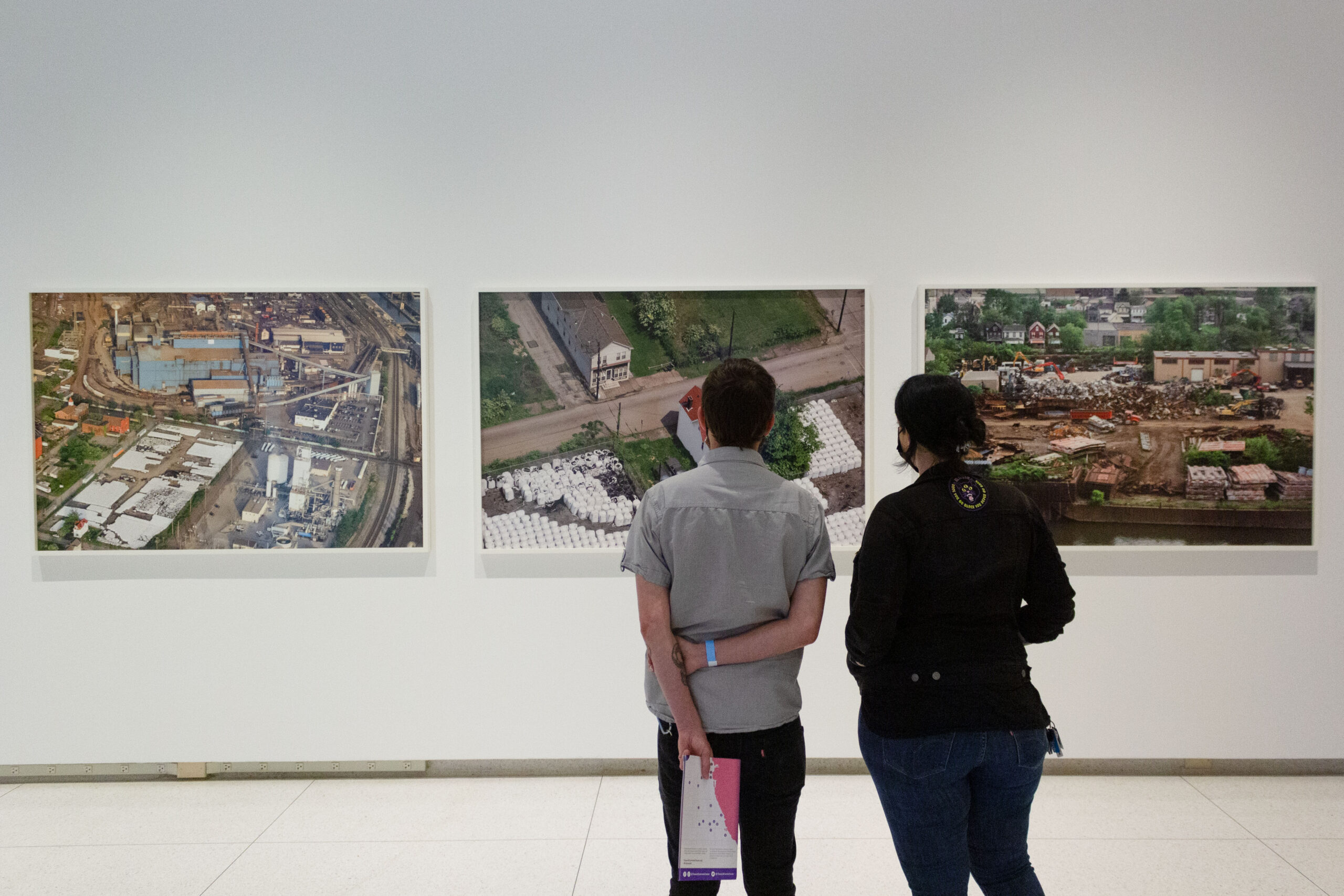 Two people looking at three large color photographs on a gallery wall