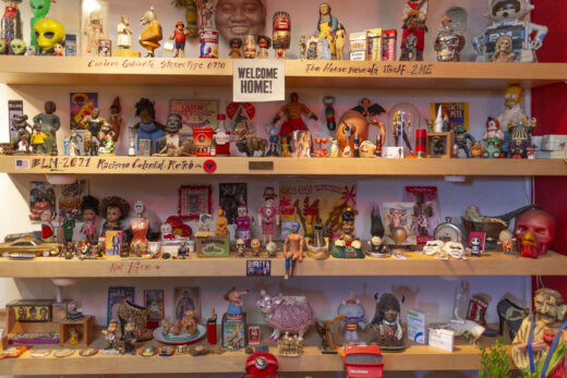 Four shelves filled with hand-held items like action figures, plastic figurines and models.