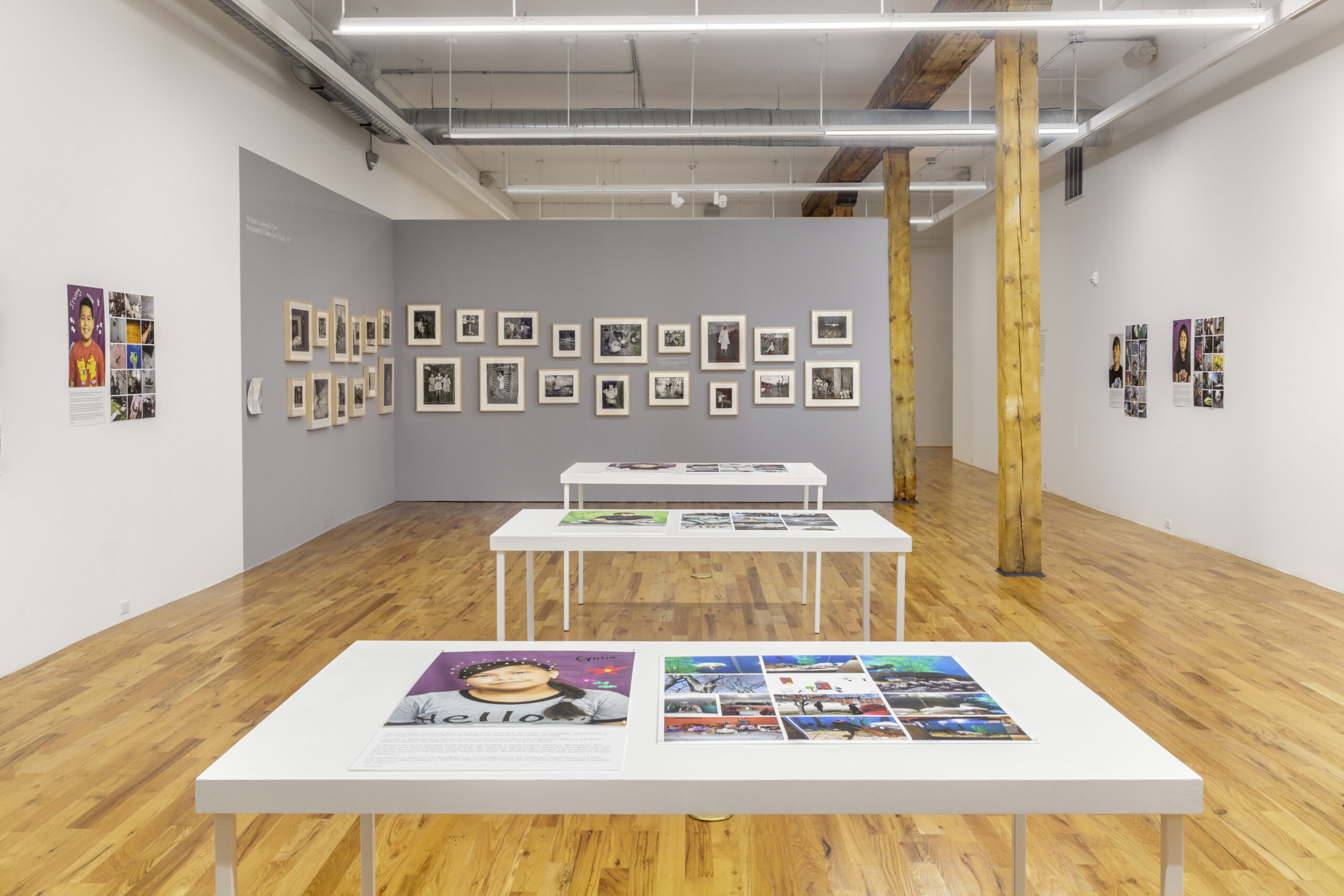 An installation featuring portraits of students, and a series of black and white photographs set against a grey wall.