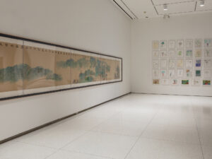 Gallery installation with framed children's drawings and a long scroll landscape painting.